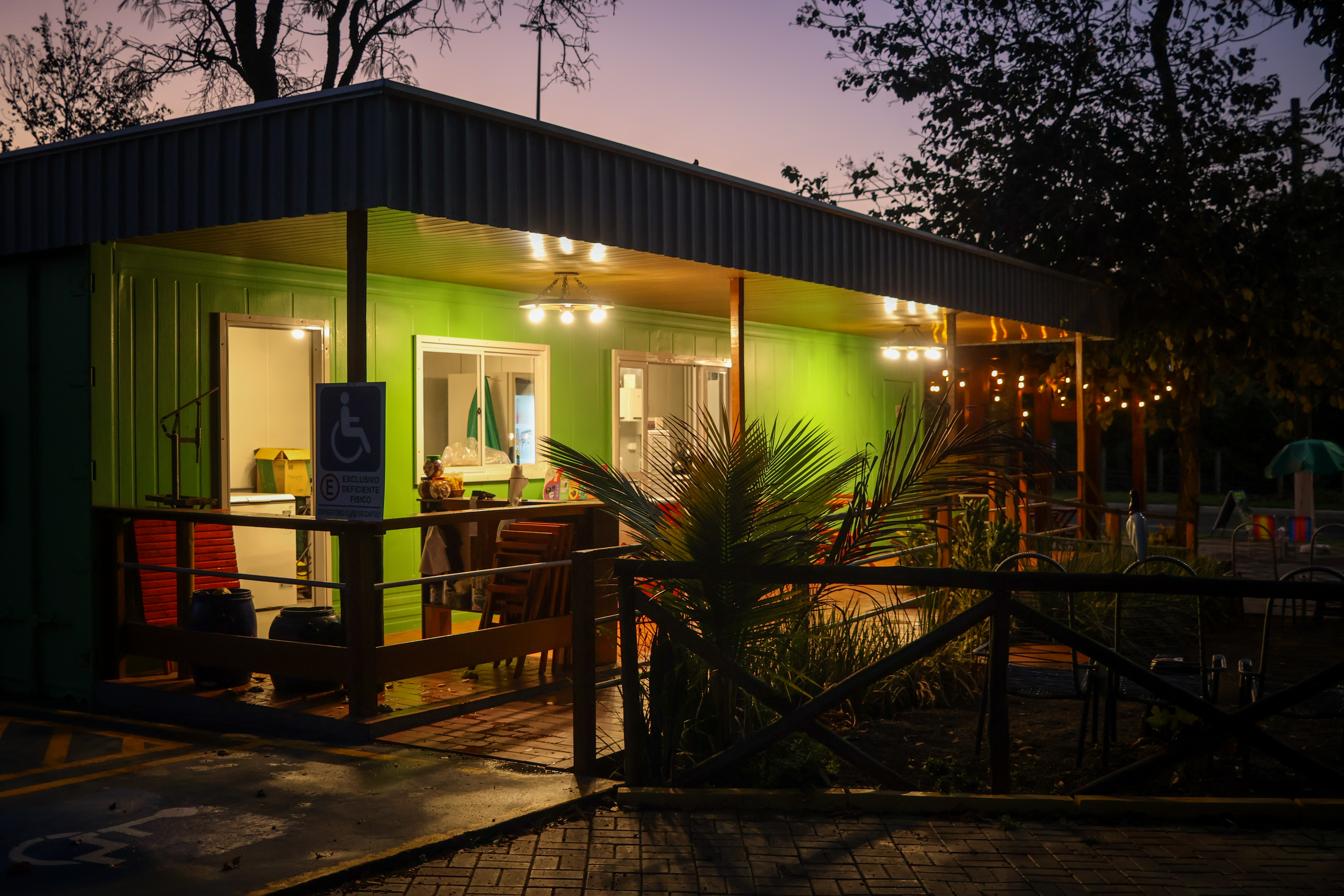 Ambiente ao ar livre do Container do Poeta próximo ao parque, com mesas e iluminação quente